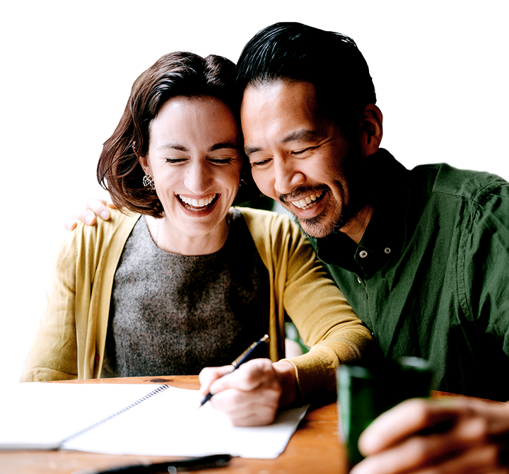 husband and wife sitting at a table with an open notebook and laughing